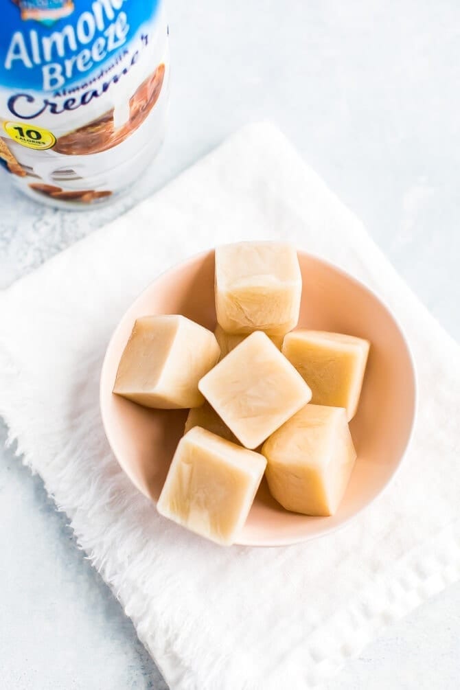 Almond Breeze almondmilk creamer bottle next to a bowl of almondmilk creamer ice cubes.