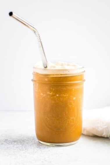 Mason jar with blended cold brew and almond milk creamer. Frothy and creamy coffee with a silver straw.