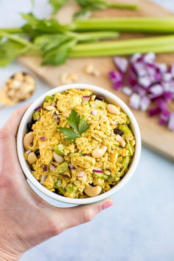 Hand holding a bowl of curry chicken salad made with cashews, celery, and red onion.