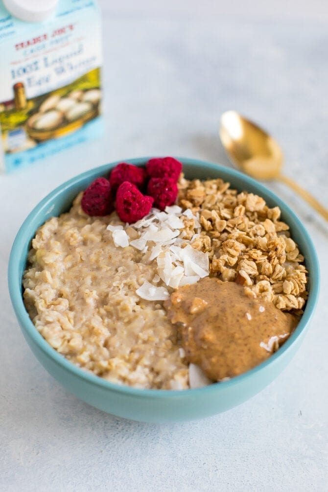 A bowl of egg white oatmeal with granola, freeze dried raspberries, coconut and almond butter.