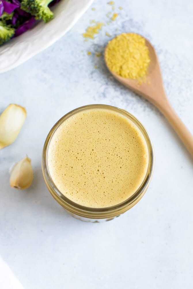 Nutritional yeast dressing in a small mason jar with garlic on the left and a spoon with nutritional yeast on the right. 