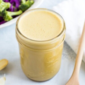 Nutritional yeast dressing in a small mason jar with garlic on the left and a spoon with nutritional yeast on the right.