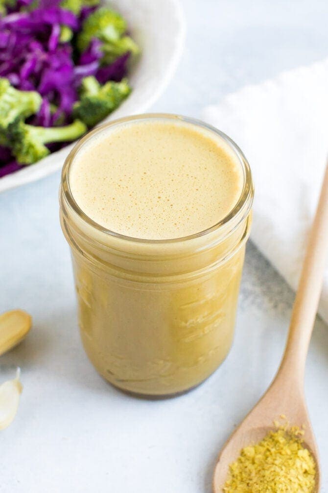 Nutritional yeast dressing in a small mason jar with garlic on the left and a spoon with nutritional yeast on the right. 