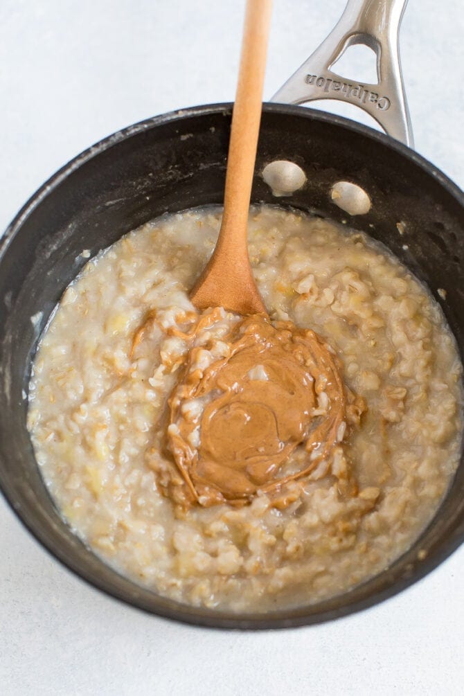 Pot of oatmeal with a wood spoon mixing in peanut butter.