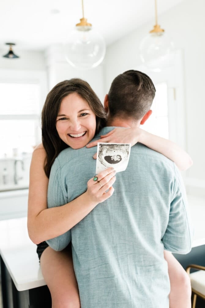 Pregnancy announcement with woman sitting on kitchen counter with man's back to the camera. 