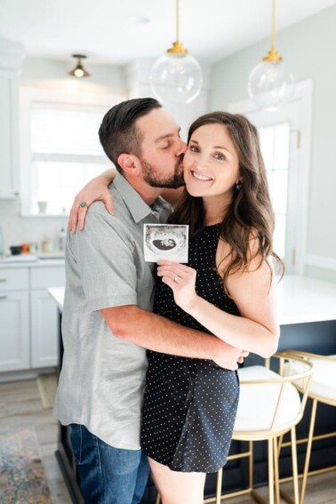 Man kissing woman on the cheek. Woman holding a sonogram photo and smiling.