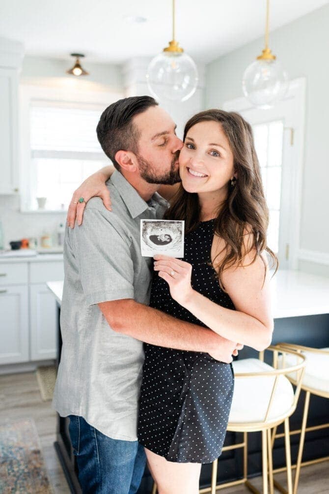 Man kissing woman on the cheek. Woman holding a sonogram photo and smiling. 
