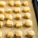 Cubes of tofu baked on a sheet pan lined with parchment paper, and coated in oat flour and nutritional yeast.