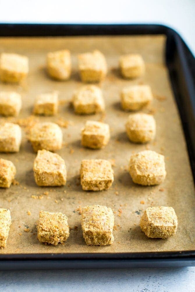 Cubes of tofu baked on a sheet pan lined with parchment paper, and coated in oat flour and nutritional yeast.