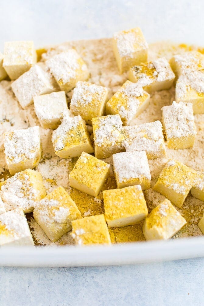 Cubes of tofu being tossed with spices, oat flour and nutritional yeast.