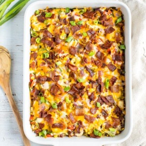 Chicken casserole in a casserole dish topped with cheese, bacon, and green onions. Spoon and onions next to baking dish.