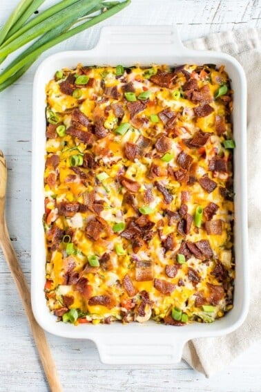 Chicken casserole in a casserole dish topped with cheese, bacon, and green onions. Spoon and onions next to baking dish.