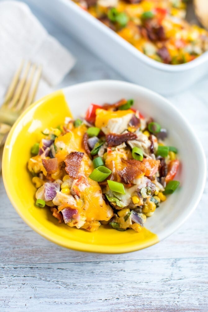 a bowl of chicken casserole made with corn, kale, cheese and bacon. topped with green onions.