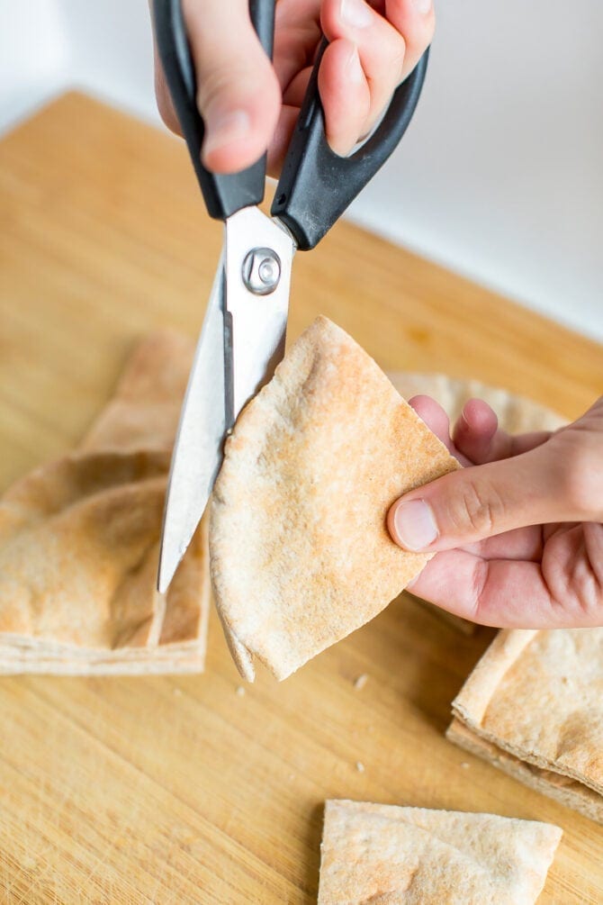 Hand cutting pita with kitchen scissors into the size for pita chips.