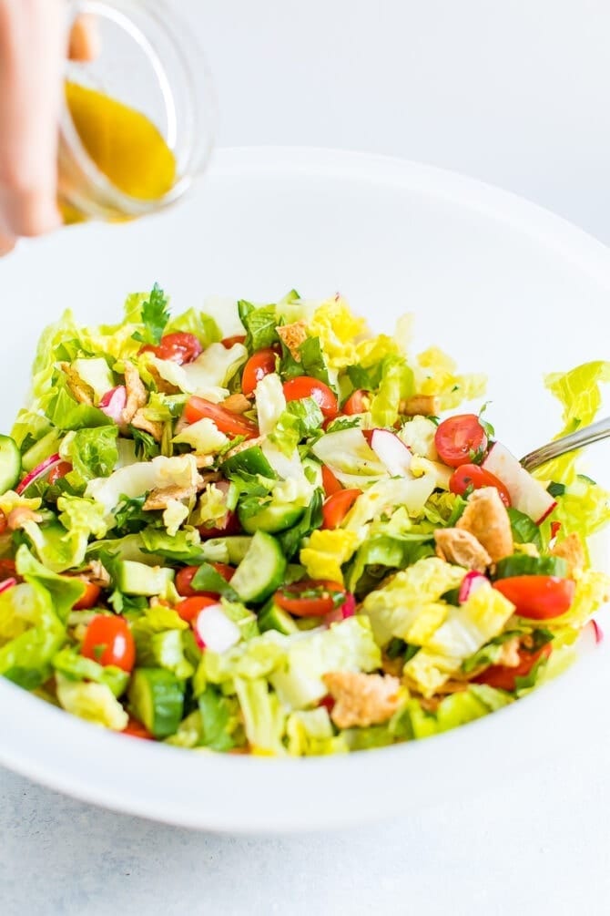 Hand pouring dressing over a bowl of fattoush salad.