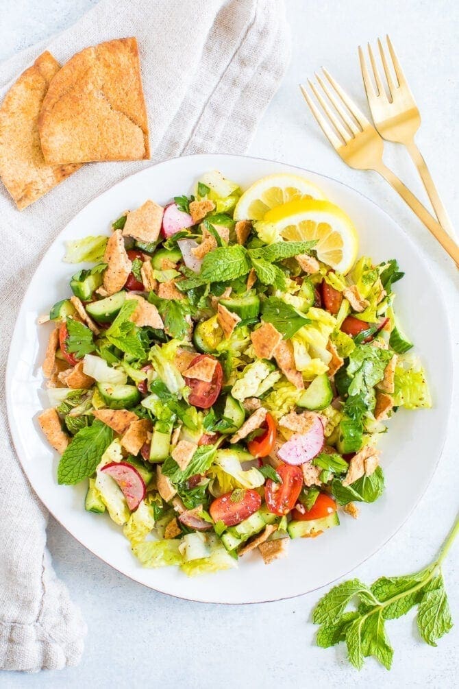 Plate of fattoush salad made with lettuce, herbs, tomato, cucumber, radishes and crumbled pita chips.