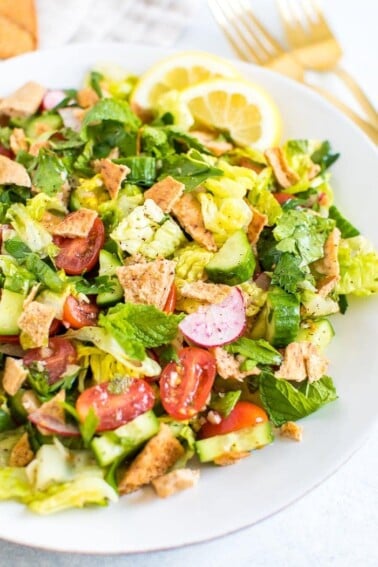 Plate of fattoush salad made with lettuce, herbs, tomato, cucumber, radishes and crumbled pita chips.