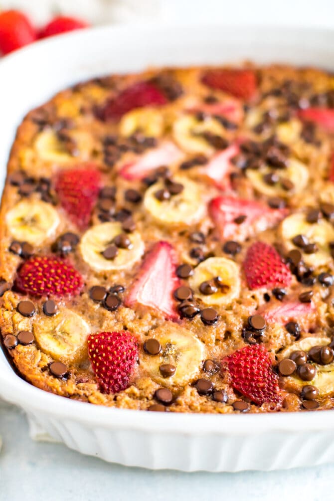 Close up shot of baked oatmeal with fresh strawberries, banana and chocolate chips in a square baking dish.