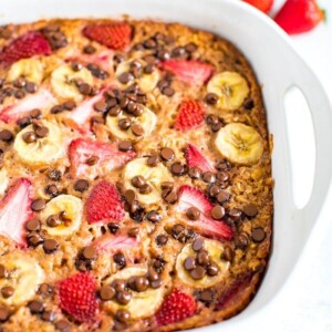 Close up shot of baked oatmeal with fresh strawberries, banana and chocolate chips in a square baking dish.