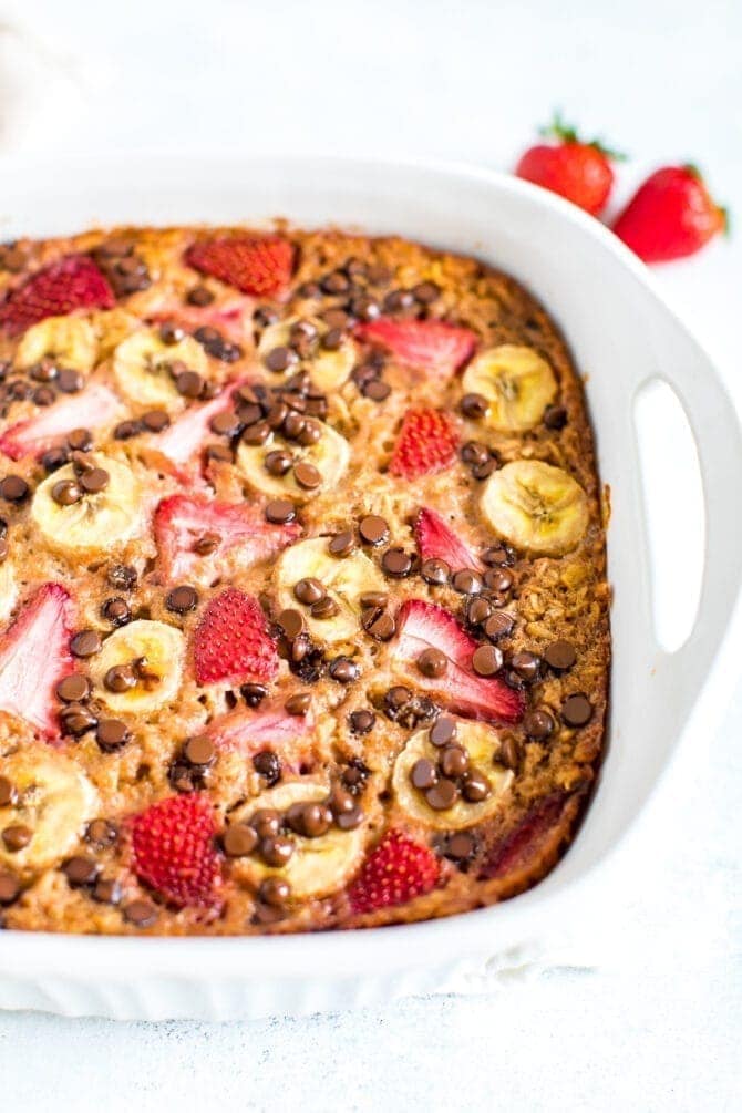 Baked oatmeal with fresh strawberries, banana and chocolate chips in a square baking dish.
