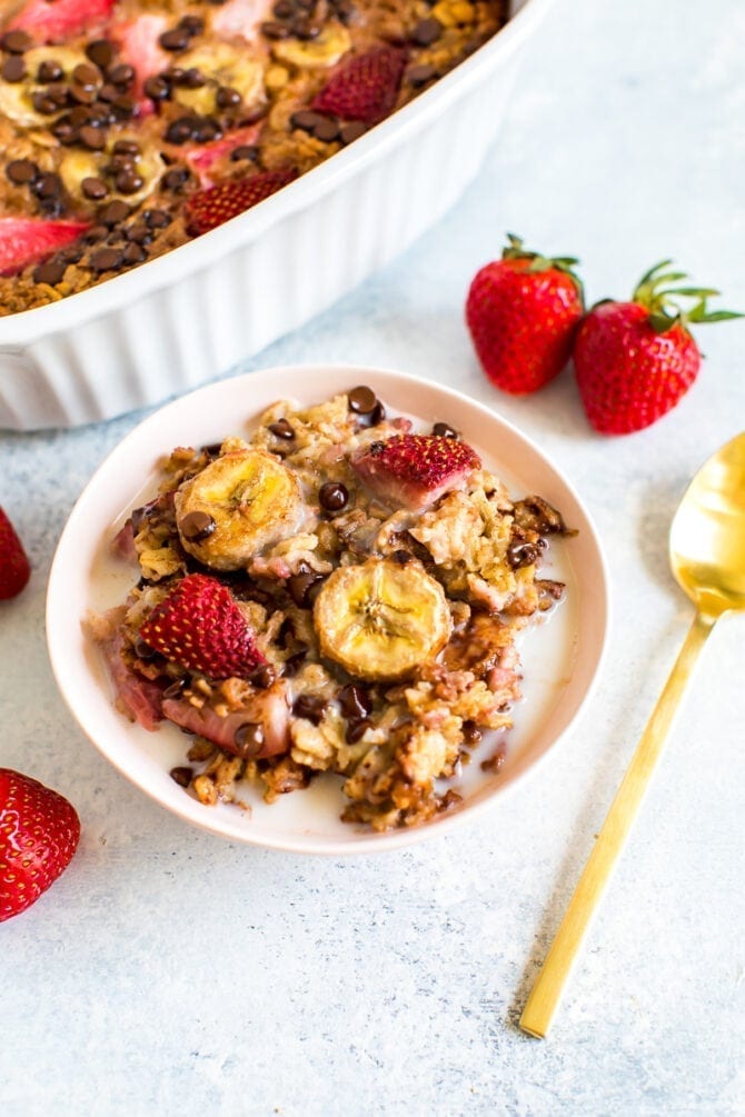 Baked oatmeal portion in a bowl with fresh strawberries, banana, chocolate chips and almond milk. 