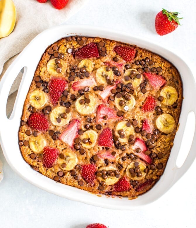 Baked oatmeal with fresh strawberries, banana and chocolate chips in a square baking dish.