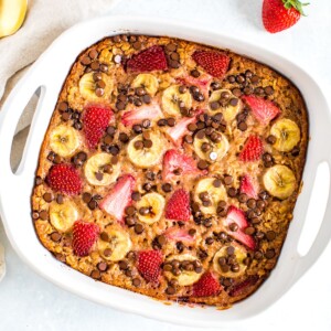 Baked oatmeal with fresh strawberries, banana and chocolate chips in a square baking dish.
