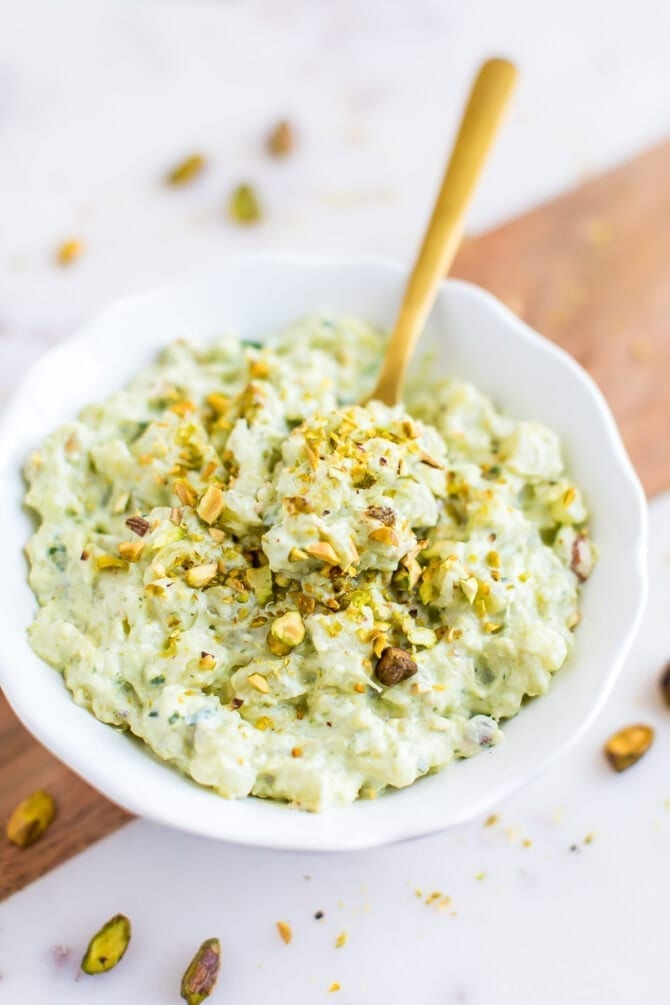 Bowl of healthy watergate salad with a gold spoon in the salad. Salad topped with chopped pistachios.