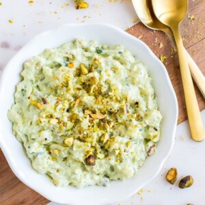 Bowl of healthy watergate salad topped with chopped pistachios. Two spoons and extra pistachios are around the bowl.