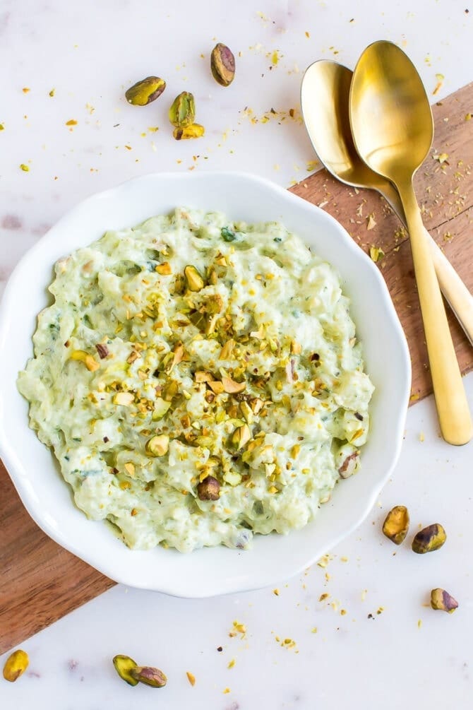 Bowl of healthy watergate salad topped with chopped pistachios. Two spoons and extra pistachios are around the bowl.