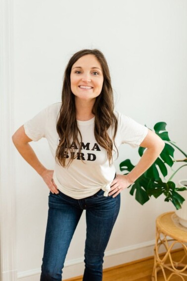 Woman smiling with her hands on her hips wearing a white shirt reading mama bird.