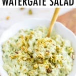 Bowl of healthy watergate salad with a gold spoon in the salad. Salad topped with chopped pistachios.