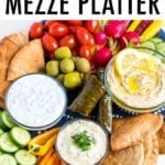 Vegetarian mezze platter with carrots, radishes, tomatoes, cucumber slices, green olives, domades, pita chips, peppers and a variety of hummus and dips.