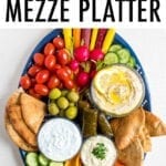 Vegetarian mezze platter with carrots, radishes, tomatoes, cucumber slices, green olives, domades, pita chips, peppers and a variety of hummus and dips.
