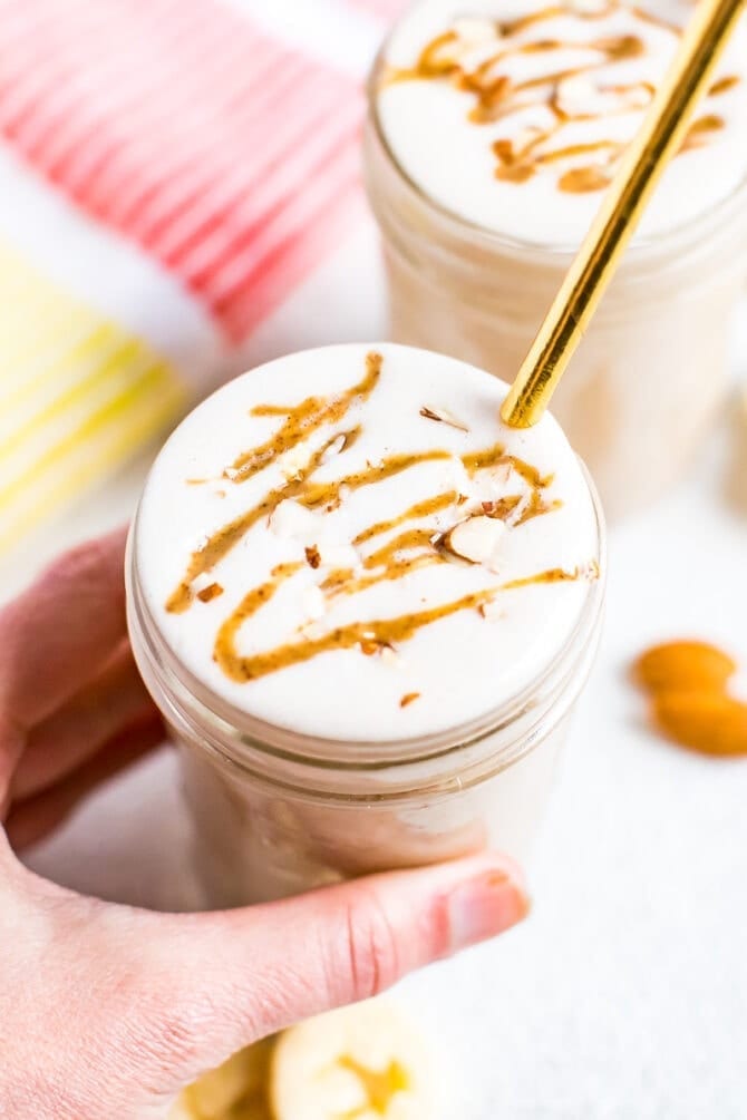 Hand holding a banana almond butter smoothie drizzled with almond butter and topped with chopped almonds.