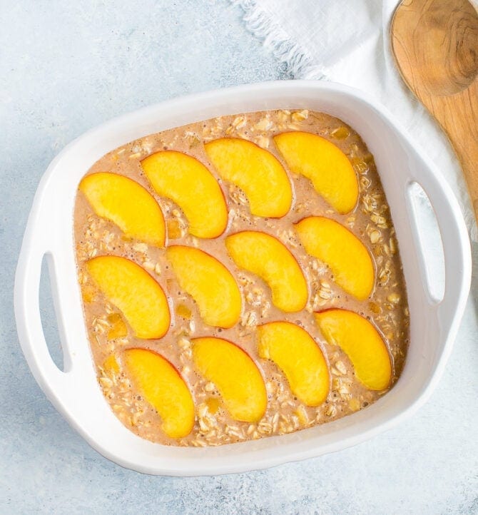 Baking dish with unbaked oatmeal topped with peach slices.