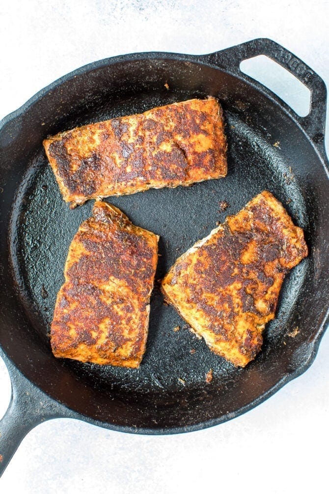 Three pieces of blackened salmon in a cast iron skillet.