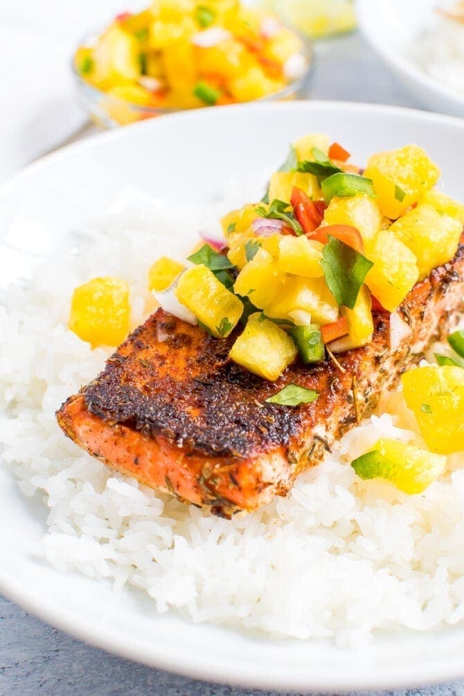 Blacked salmon topped with pineapple salsa and sitting on top of a plate of rice.