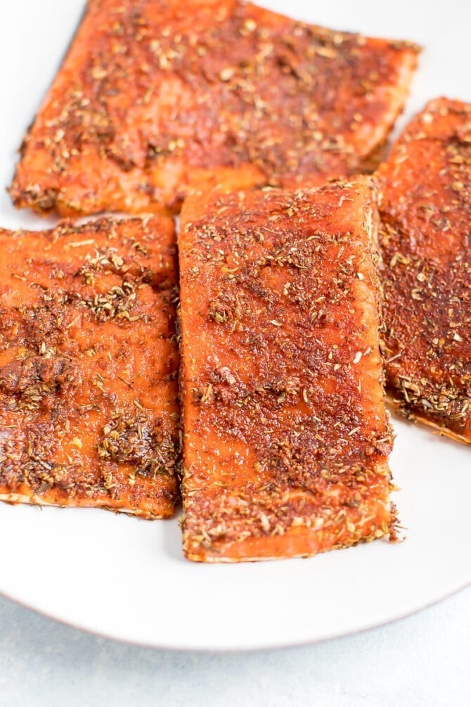 Four pieces of uncooked salmon rubbed with blacked seasoning.