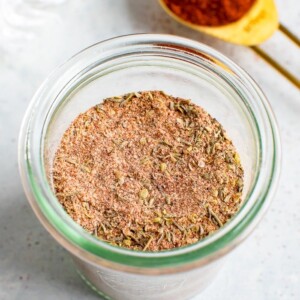 Glass jar with blackened seasoning. A teaspoon of paprika is in the background.