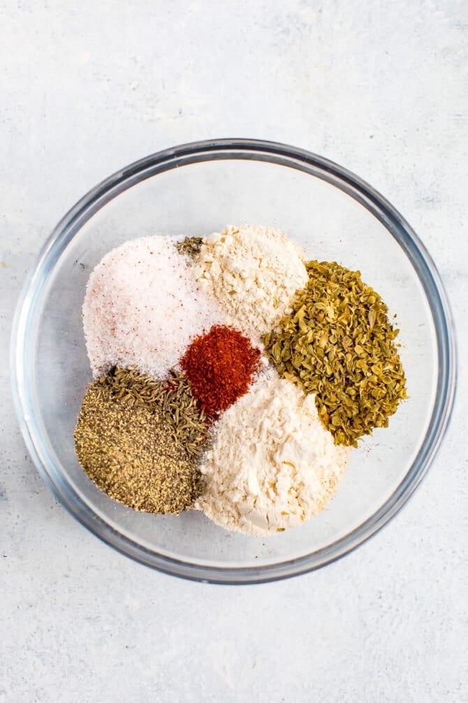 Glass bowl with spices for blackening seasoning before being mixed. Spices are salt, pepper, onion powder, garlic powder, oregano, and paprika.