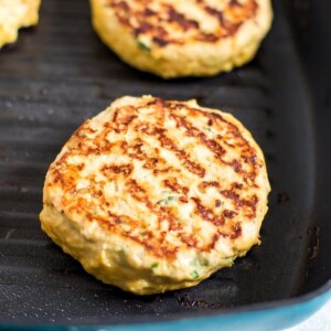 Chicken burgers cooking in a grill pan on the stove.