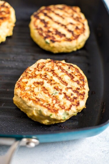 Chicken burgers cooking in a grill pan on the stove.