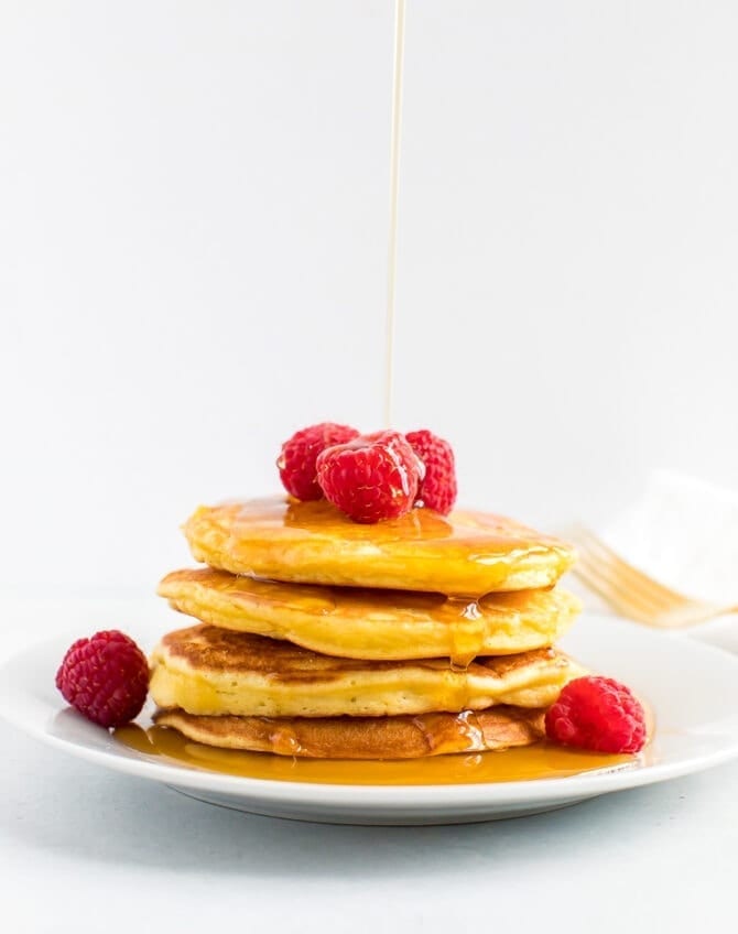 Stack of coconut flour pancakes topped with raspberries and being drizzled with maple syrup.