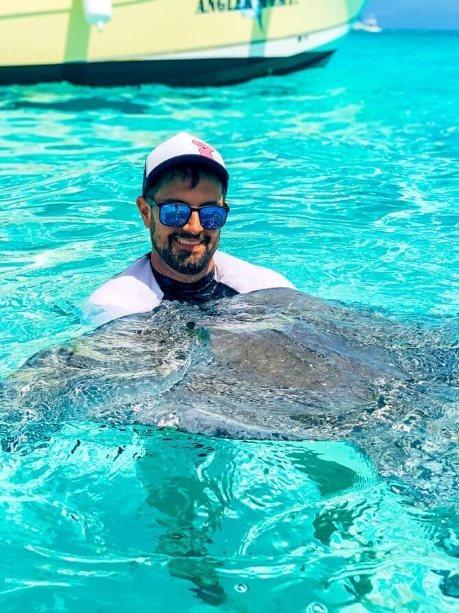 Man smiling in the Caribbean water with a stingray.
