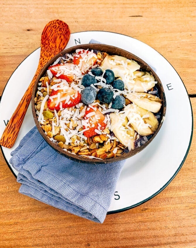 Smoothie bowl topped with granola, strawberries, banana, blueberries and coconut.
