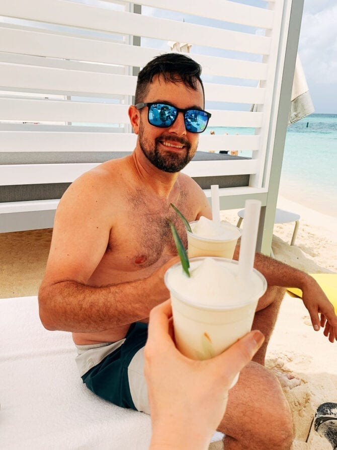 Two people cheersing pina coladas in a cabana on the beach.