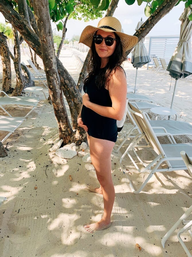 Woman in beach attire holding a pregnant belly with her hands.