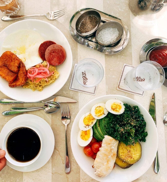 Two plates of food at a restaurant-- eggs, veggies, meat and fish.