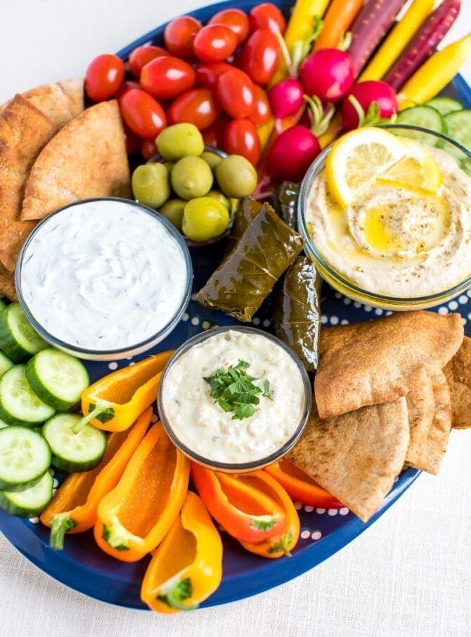 Vegetarian mezze platter with carrots, radishes, tomatoes, cucumber slices, green olives, domades, pita chips, peppers and a variety of hummus and dips.